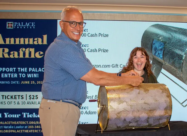 a man and woman behind a raffle ticket drum