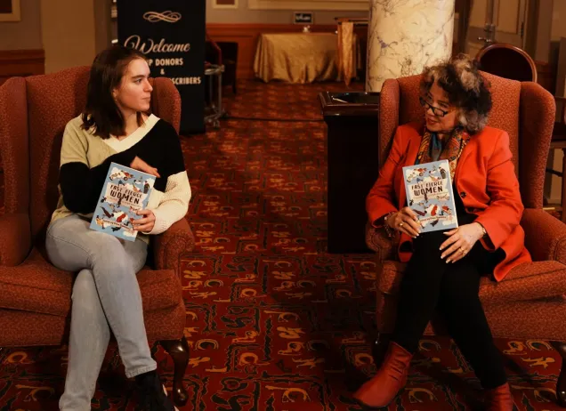 Two women sitting in armchairs holding books